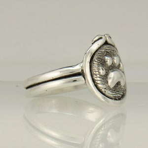 May include: Silver ring with a paw print design. The ring is double-banded and has a textured finish.