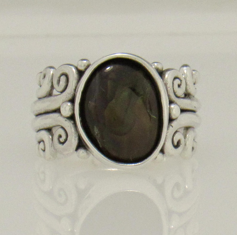 Op de afbeelding: Een zilveren ring met een donkergroene ovale edelsteen, gezet in een zwierig, versierd ontwerp.