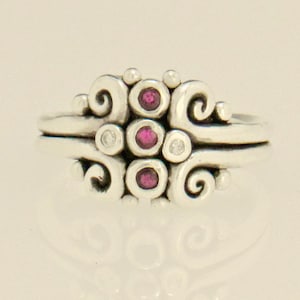 May include: A silver ring with a swirling design and three pink gemstones set in the center.