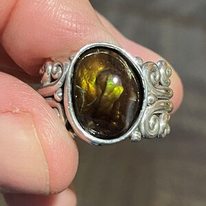 Op de afbeelding: Een zilveren ring met een grote, ovale, bruin en groene agaat edelsteen gezet in een decoratief, scroll-achtig ontwerp.
