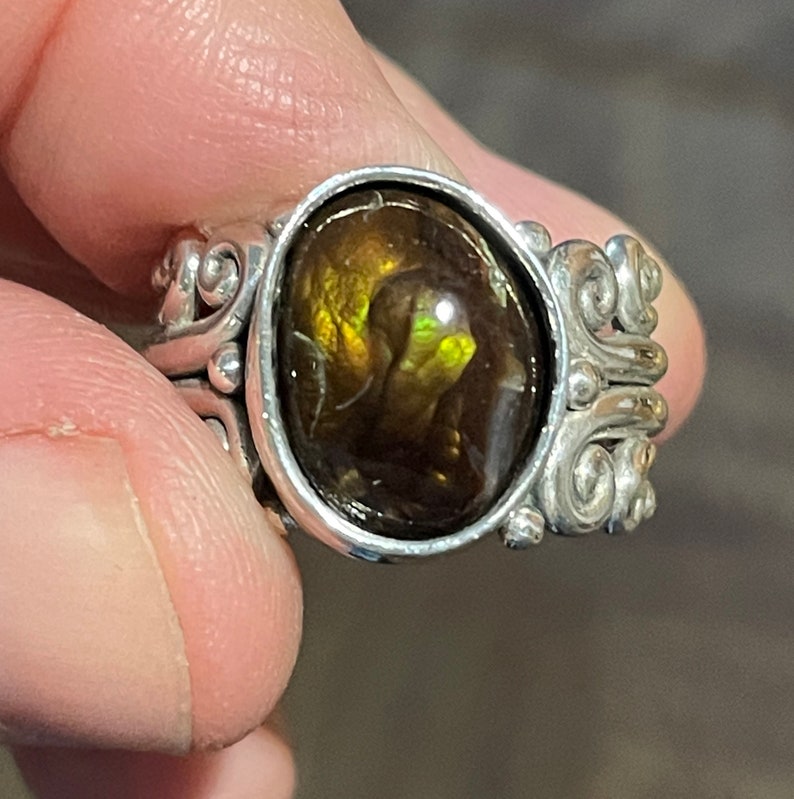 Op de afbeelding: Een zilveren ring met een grote, ovale, bruin en groene agaat edelsteen gezet in een decoratief, scroll-achtig ontwerp.