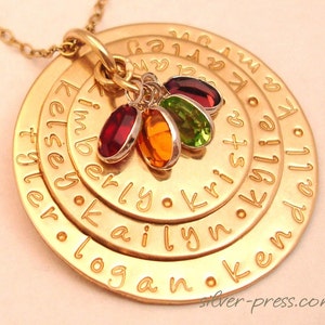 May include: Gold necklace with multiple circular pendants engraved with names, including "Kelsey", "Logan", "Kailyn", "Krista", "Kimberly", and "Kendall".  Each pendant has a small gemstone charm in red, orange, green, and purple.