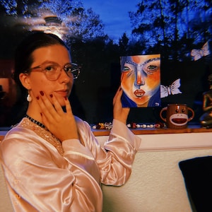 May include: A rectangular canvas painting featuring a stylized portrait with vibrant orange, blue, and white tones. The artwork displays a face with prominent eyes and lips, signed with the initials JD in the bottom right corner of the canvas.