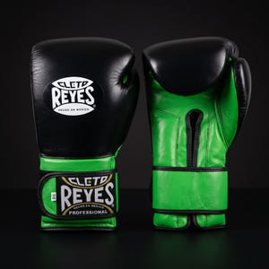 May include: A pair of black and green boxing gloves. The gloves feature a black upper section and green wrist and palm areas. The brand name "CLETO REYES" is displayed in white lettering. The gloves are designed for professional use.