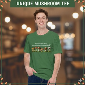 May include: Green t-shirt with the text "UNIQUE MUSHROOM TEE" at the top. The shirt features a row of illustrated mushrooms and the quote, "If I were human, I'd connect with everyone." The model is wearing the shirt.