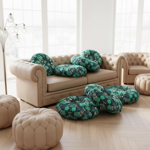 Könnte beinhalten: Ein Wohnzimmer mit beigem Sofa und Ottomanen sowie runden Kissen mit einem dunkelblauen Blumenmuster. Die Kissen sind auf dem Sofa und dem Boden verstreut. Der Raum hat große Fenster und eine moderne Stehlampe.