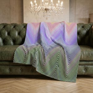 May include: A soft throw blanket featuring a vibrant chevron pattern with a gradient of colors transitioning from deep forest green at the bottom to bright purple, pink, and yellow hues at the top, composed of thin, repeating diagonal white lines.