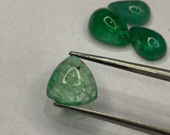 May include: A collection of polished emerald gemstones in various shapes. One triangular emerald is held by tweezers, showcasing its translucent green color. Other emeralds are teardrop-shaped, with a glossy finish.