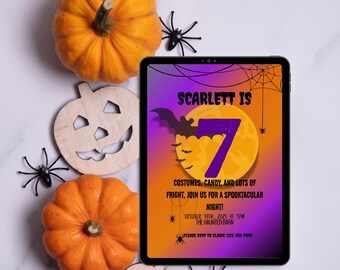 May include: A Halloween-themed invitation on a tablet, featuring the text "Scarlett is 7" with a bat and moon graphic. Orange pumpkins, a wooden jack-o'-lantern, and plastic spiders surround the tablet, creating a festive atmosphere.