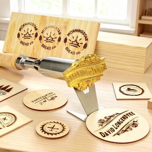 Op de afbeelding: Een houtbrandstempel met een decoratieve goudkleurige kop en een houten handvat, samen met diverse houten onderzetters en een houten bord. Het bord en de onderzetters hebben gegraveerde teksten en ontwerpen, waaronder de woorden "MORNINGSTAR BREAD CO."