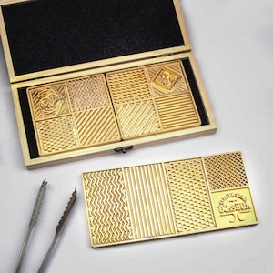 May include: A wooden storage box with black foam lining containing gold-colored metal plates with various geometric textures. A separate rectangular gold-colored metal plate features wavy, striped, honeycomb, and grid patterns with the text ROE & CO.