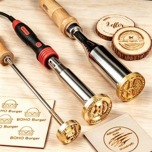 Peut inclure: Trois fers à marquer avec des manches en bois et des têtes métalliques aux motifs circulaires. Un fer possède un élément chauffant électrique noir et rouge. Deux tranches de bois circulaires portent des logos brûlés et deux carrés de bois présentent des graphismes de burger et de griffes.