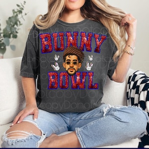 May include: Dark gray t-shirt with the text "BUNNY BOWL" in red glitter letters with a blue outline. The shirt features a graphic of a man wearing sunglasses and a hat, surrounded by white bunny faces.