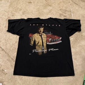 May include: Black t-shirt featuring a graphic of Joe Diffie in a tan shirt and a red pickup truck. The text "JOE DIFFIE" is above the image, and "Pickup Man" is below.