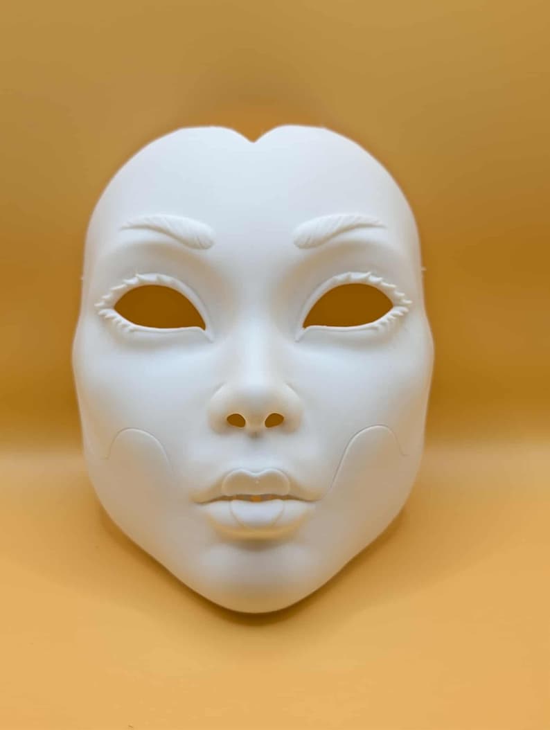 May include: A blank, white mask with a human face design. The mask features eye holes, a nose, and a mouth. The eyebrows and eyelashes are also detailed. The mask is likely for costume or decorative purposes.