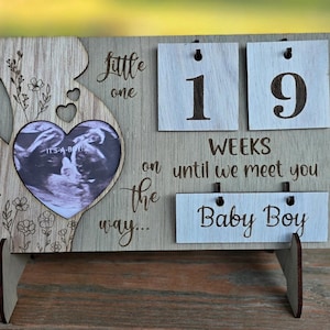 May include: Wooden pregnancy announcement sign with a heart-shaped sonogram photo. The sign displays "little one on the way..." and "19 weeks until we meet you Baby Boy."