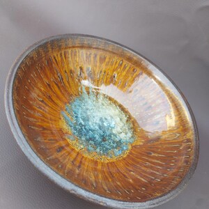 Puede incluir: Un cuenco de cerámica ovalado con acabado brillante. El cuenco presenta un exterior marrón y dorado con una zona central turquesa. El borde es de color marrón oscuro, creando un borde contrastante. El diseño del cuenco es orgánico y visualmente atractivo.