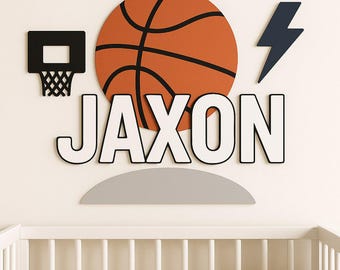 Könnte beinhalten: Wanddekoration im Basketball-Design mit einem orange-schwarzen Basketball, einem schwarzen Korb, einem marineblauen Blitz und dem Namen "JAXON" in weißen Buchstaben mit schwarzen Umrissen. Darunter befindet sich ein graues Regal.