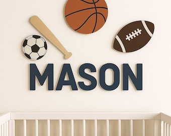 May include: Wall decor featuring a basketball, soccer ball, baseball bat, and football. The name "MASON" is spelled out in navy blue letters. The decor is above a white crib.