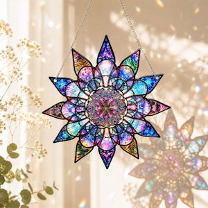 May include: A decorative stained glass suncatcher in a starburst shape. The design features a kaleidoscope of colours, including blues, purples, pinks, and greens. It is suspended by a silver chain and is designed to catch the light.