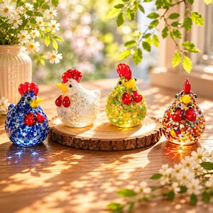 Può includere: Quattro piccole statuette di pollo in vetro con creste e bargigli rossi. Una è blu con macchie bianche, una bianca con macchie dorate, una verde con punti gialli e arancioni, e una multicolore con coriandoli rossi, blu, gialli e bianchi.