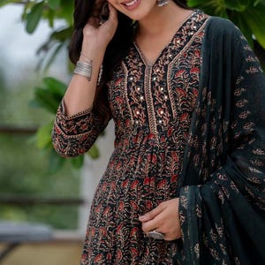 May include: A black and red floral print dress with a V-neckline, embellished with small mirrors. The dress has long sleeves and is paired with a dark green scarf. The fabric has a detailed floral pattern. The dress is a traditional style.