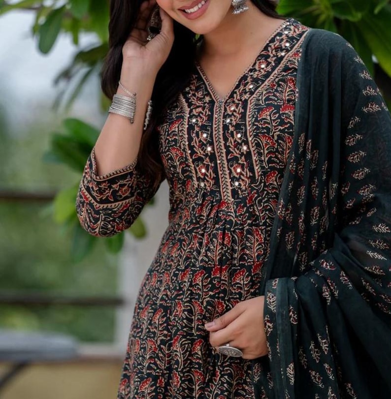 May include: A black and red floral print dress with a V-neckline, embellished with small mirrors. The dress has long sleeves and is paired with a dark green scarf. The fabric has a detailed floral pattern. The dress is a traditional style.