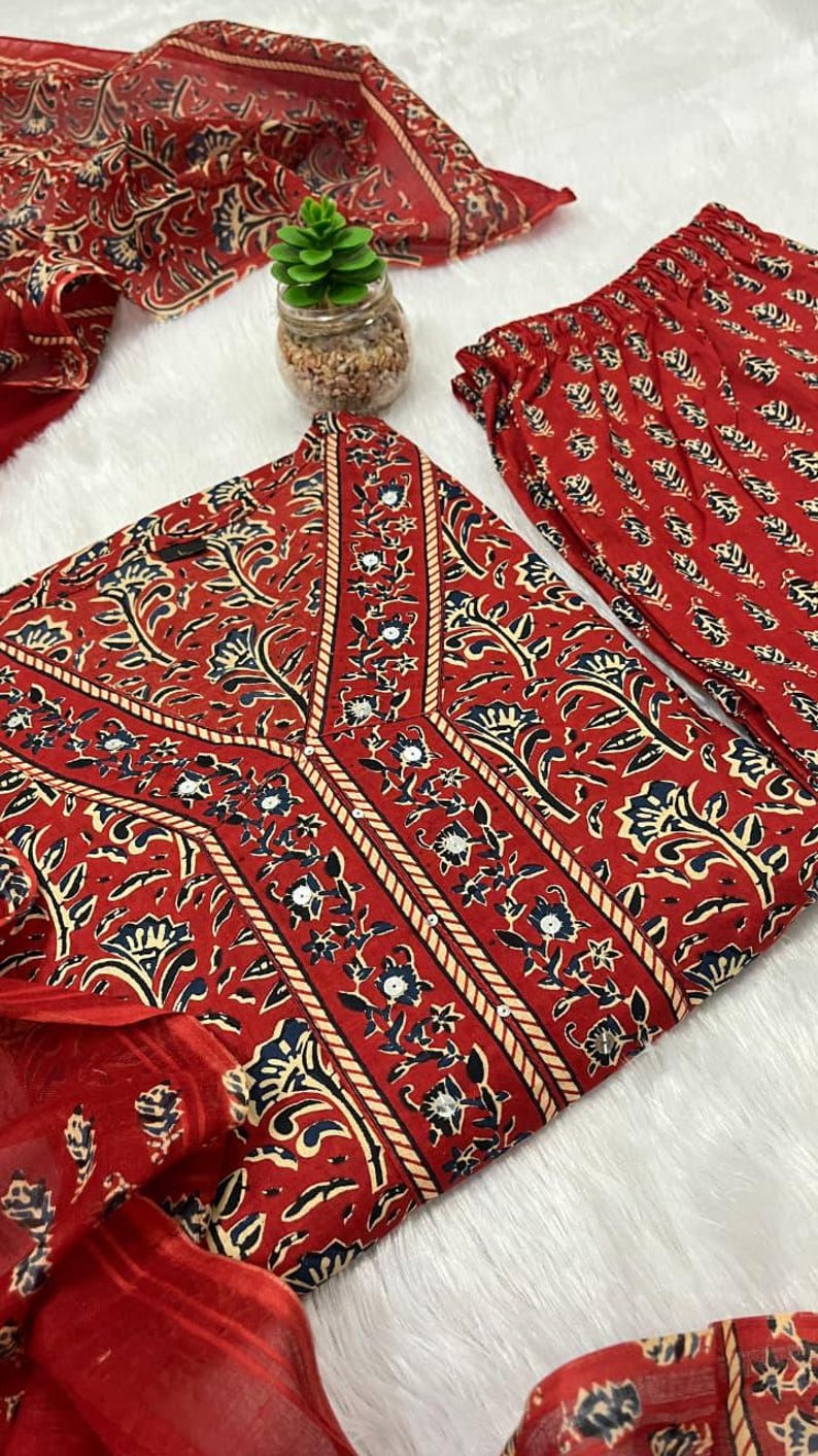 May include: A red floral print outfit, including a top, pants, and scarf. The top features a V-neck design with cream-colored trim and a repeating floral pattern in navy and white. The pants and scarf have a similar repeating pattern. The fabric appears soft.