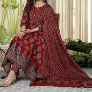 Può includere: Un completo salwar kameez indiano stampato in rosso. L'outfit include una lunga tunica, pantaloni abbinati e uno scialle. Il tessuto presenta un motivo paisley e geometrico nei toni del rosso, blu e bianco. La tunica ha uno scollo tondo e maniche a tre quarti.