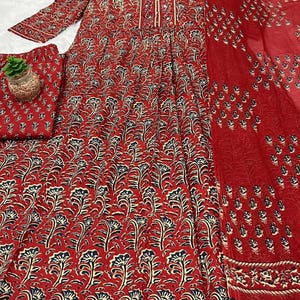 May include: A red floral print dress with matching pants and a scarf. The dress features a V-neck and long sleeves. The floral pattern includes black and cream-colored accents. The fabric appears lightweight and suitable for warm weather.