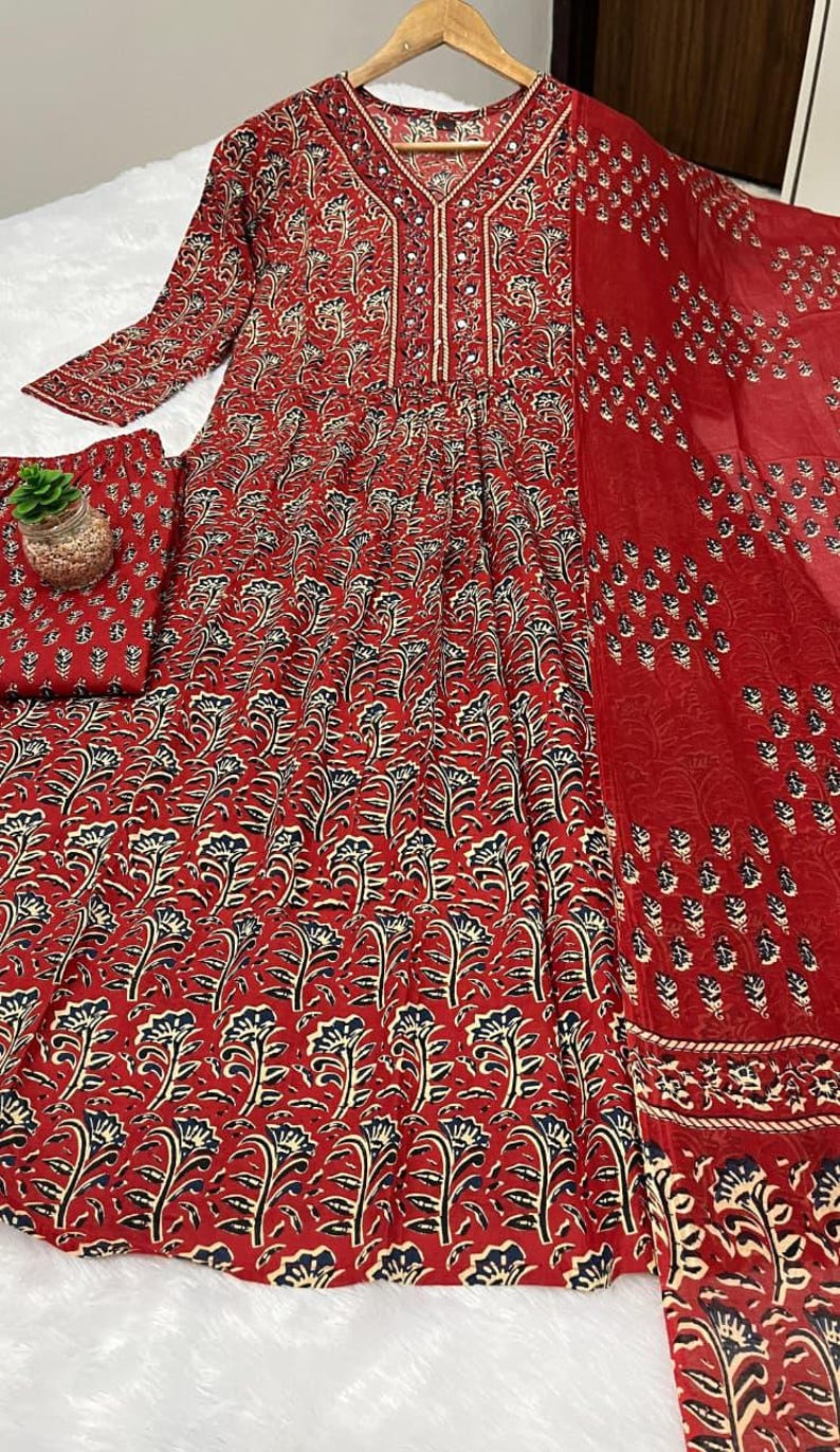 May include: A red floral print dress with matching pants and a scarf. The dress features a V-neck and long sleeves. The floral pattern includes black and cream-colored accents. The fabric appears lightweight and suitable for warm weather.