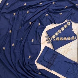 May include: A navy blue three-piece outfit featuring a top, pants, and a draped fabric. The top and pants have gold embroidery. The top has a floral design around the neckline and tassels. The pants have a lace trim.