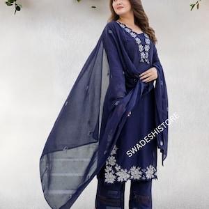 May include: A navy blue salwar kameez set with white floral embroidery. The ensemble includes a long-sleeved tunic, matching pants, and a sheer dupatta. The text "SWADESHISTORE" is visible on the image.