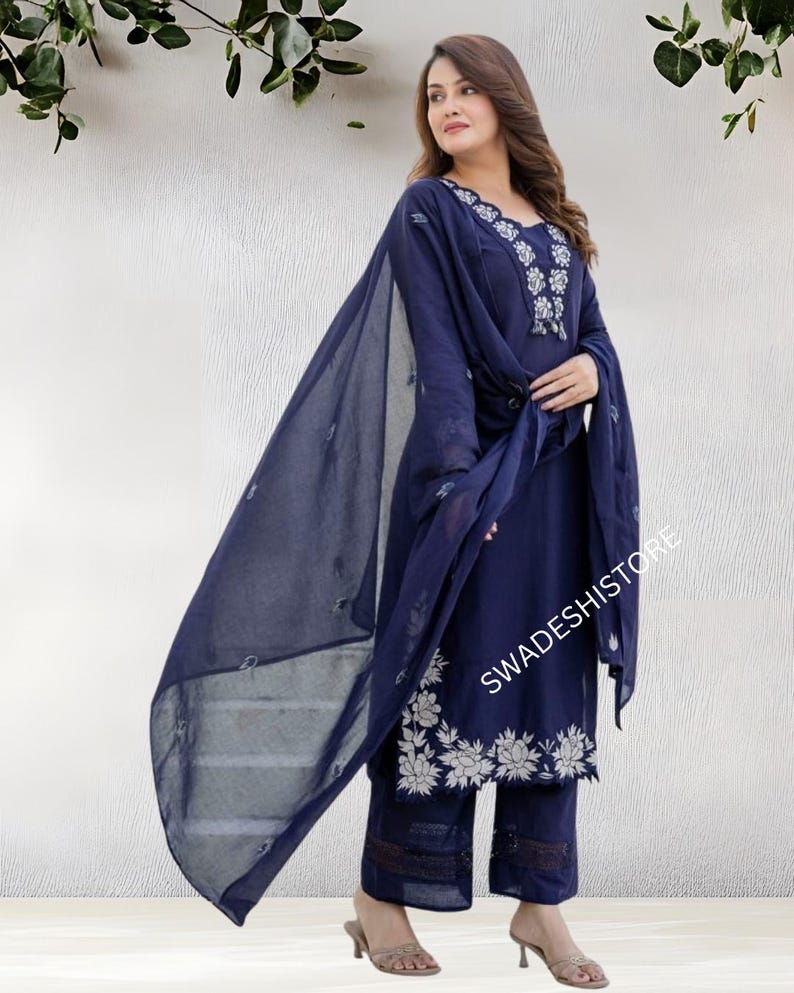 May include: A navy blue salwar kameez set with white floral embroidery. The ensemble includes a long-sleeved tunic, matching pants, and a sheer dupatta. The text "SWADESHISTORE" is visible on the image.