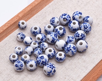Puede incluir: Un conjunto de cuentas de cerámica blanca con un patrón floral azul. Estas cuentas redondas, con un agujero central, son ideales para la creación de joyas u objetos decorativos. El diseño floral azul es detallado y cubre la superficie de las cuentas.