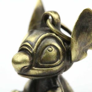May include: A bronze-colored keychain featuring a detailed, stylized character head with large ears and a prominent nose. The keychain has a ring for attachment. The design is reminiscent of a popular animated character.