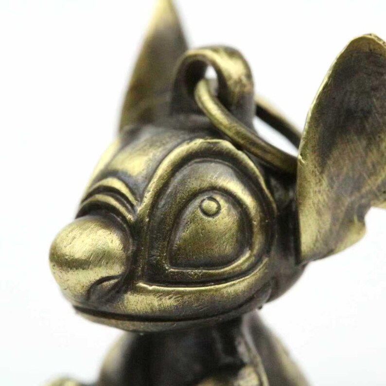 May include: A bronze-colored keychain featuring a detailed, stylized character head with large ears and a prominent nose. The keychain has a ring for attachment. The design is reminiscent of a popular animated character.