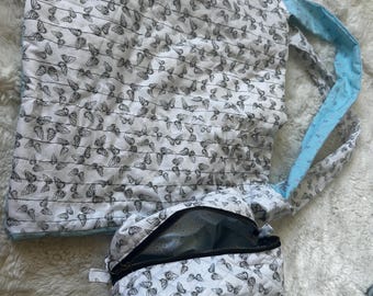 May include: A white quilted tote bag and matching zippered pouch, both adorned with a repeating black butterfly pattern. The tote features light blue accents on the straps and edges, while the pouch has a black zipper.