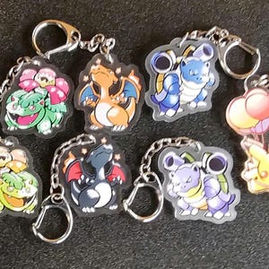 Puede incluir: Llaveros variados de personajes de Pokémon. Los llaveros presentan varios Pokémon, como Bulbasaur, Charizard, Blastoise y Pikachu. Cada llavero tiene una cadena plateada y un cierre metálico. Los llaveros están hechos de plástico transparente.