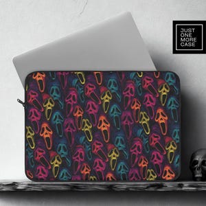 Może przedstawiać: Etui na laptopa z powtarzającym się wzorem kolorowych masek duchów na czarnym tle. Maski są obrysowane neonowymi kolorami, w tym żółtym, pomarańczowym, różowym i niebieskim. Etui jest częściowo otwarte, odsłaniając laptopa.