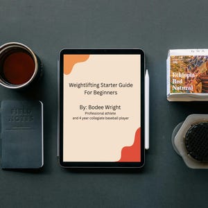 May include: An overhead shot of a dark surface with a tablet displaying "Weightlifting Starter Guide For Beginners", a pen, a notebook, a coffee cup, a coffee filter, and a box of "Ethiopia Red Natural" coffee.