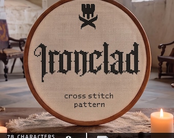 Op de afbeelding: Een ronde houten borduurring met beige stof en een zwart kruissteekpatroon. De tekst luidt Ironclad met een klein embleem erboven en de woorden cross stitch pattern eronder. Onderaan staat tekst over 78 tekens.