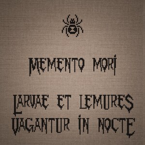 May include: A cross-stitch embroidery on a light brown fabric background featuring a black spider icon at the top. Below the spider, the text reads MEMENTO MORI, followed by the Latin phrase LARVAE ET LEMURES VAGANTUR IN NOCTE in black thread.