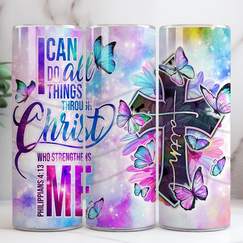 May include: A stainless steel tumbler with a wraparound design featuring a cross, butterflies, and floral elements. The tumbler has the text "I Can Do All Things Through Christ Who Strengthens Me" and "Faith". The background is a watercolour wash of purple, blue, and pink.