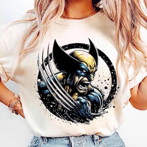 May include: Cream-colored t-shirt featuring a graphic of Wolverine with his claws extended. The illustration is in shades of blue, yellow, and black, set within a black circle with a splatter effect.