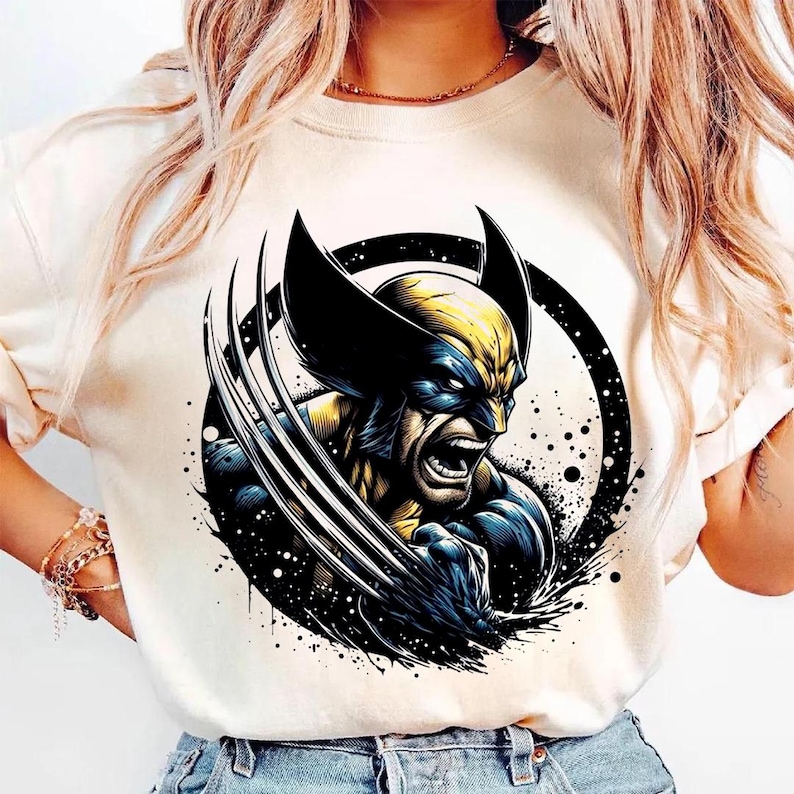 May include: Cream-colored t-shirt featuring a graphic of Wolverine with his claws extended. The illustration is in shades of blue, yellow, and black, set within a black circle with a splatter effect.