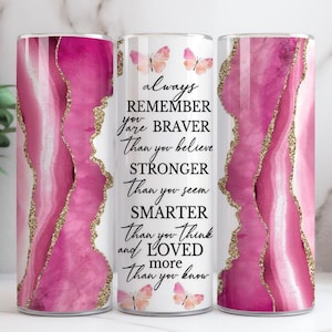May include: A cylindrical tumbler featuring a pink and gold agate pattern. The tumbler is inscribed with the words "always remember you are braver than you believe, stronger than you seem, smarter than you think and loved more than you know".