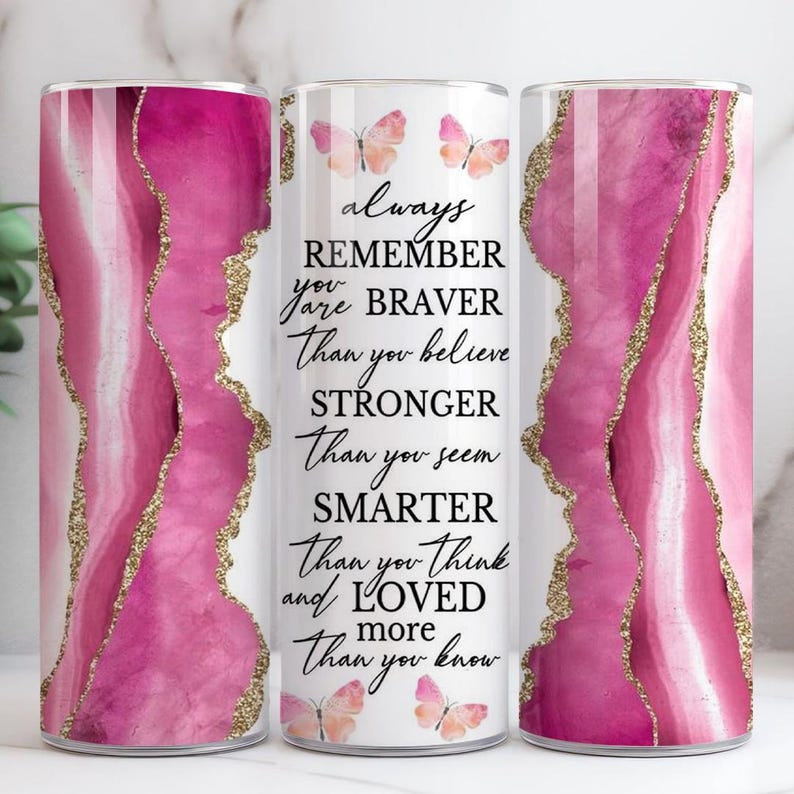 May include: A cylindrical tumbler featuring a pink and gold agate pattern. The tumbler is inscribed with the words "always remember you are braver than you believe, stronger than you seem, smarter than you think and loved more than you know".