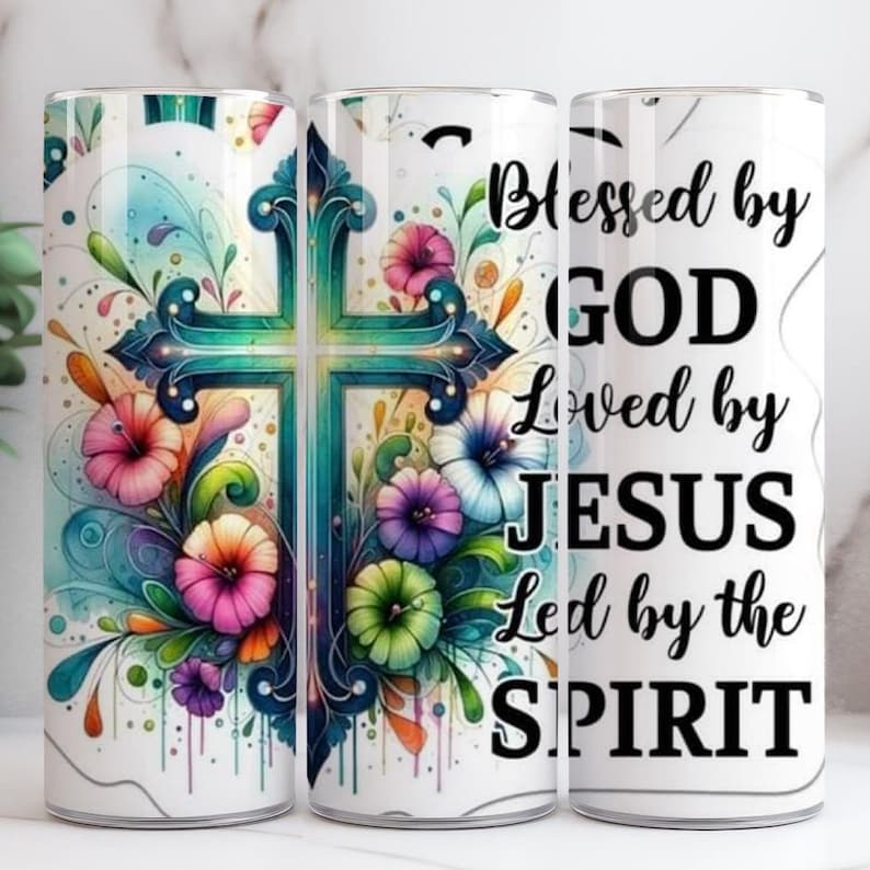 May include: A white tumbler with a teal cross design and colourful flowers. The tumbler has the words "Blessed by GOD Loved by JESUS Led by the SPIRIT" in black script.