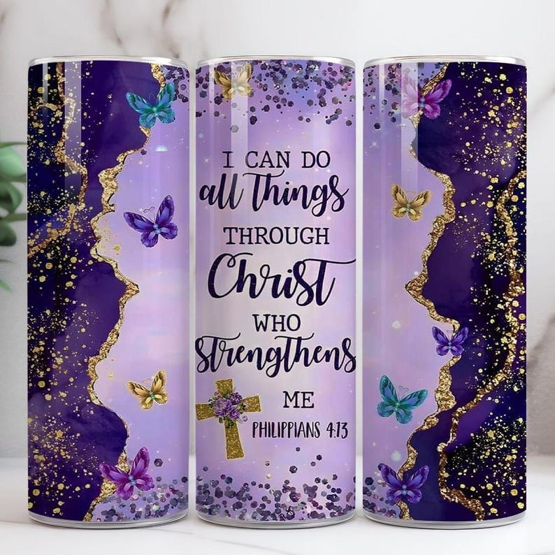 May include: A purple and gold tumbler with a design featuring butterflies and the text "I CAN DO all THINGS THROUGH CHRIST WHO STRENGTHENS ME PHILIPPIANS 4:13". The tumbler has a gold glitter design.